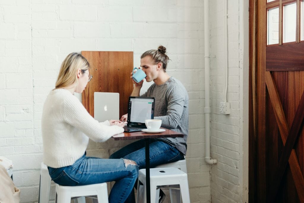 Two people sitting with poor posture while working on laptops, demonstrating common workplace ergonomic issues