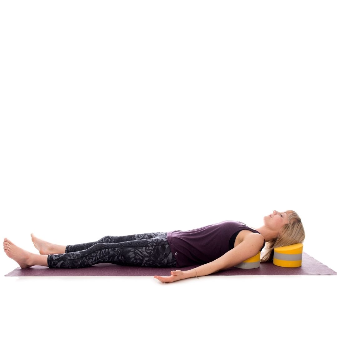 A young lady demonstrates Supported Corpse Pose (Savasana) using a Standard Buttafly under her shoulder blades and a Tall Buttafly under the head for a comfort and deep relaxation.