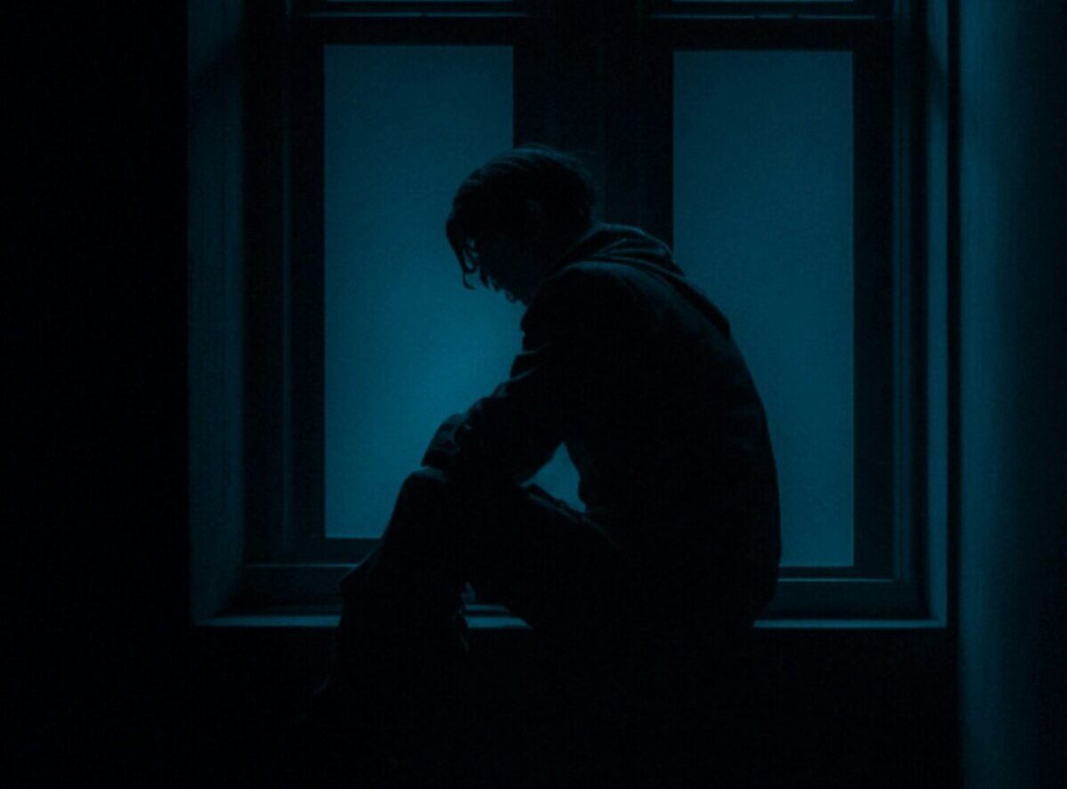 Artistic photo of a man in low lighting with a slumped, defeated posture, visually expressing mid-thoracic pain and the emotional weight of defeat and humiliation.