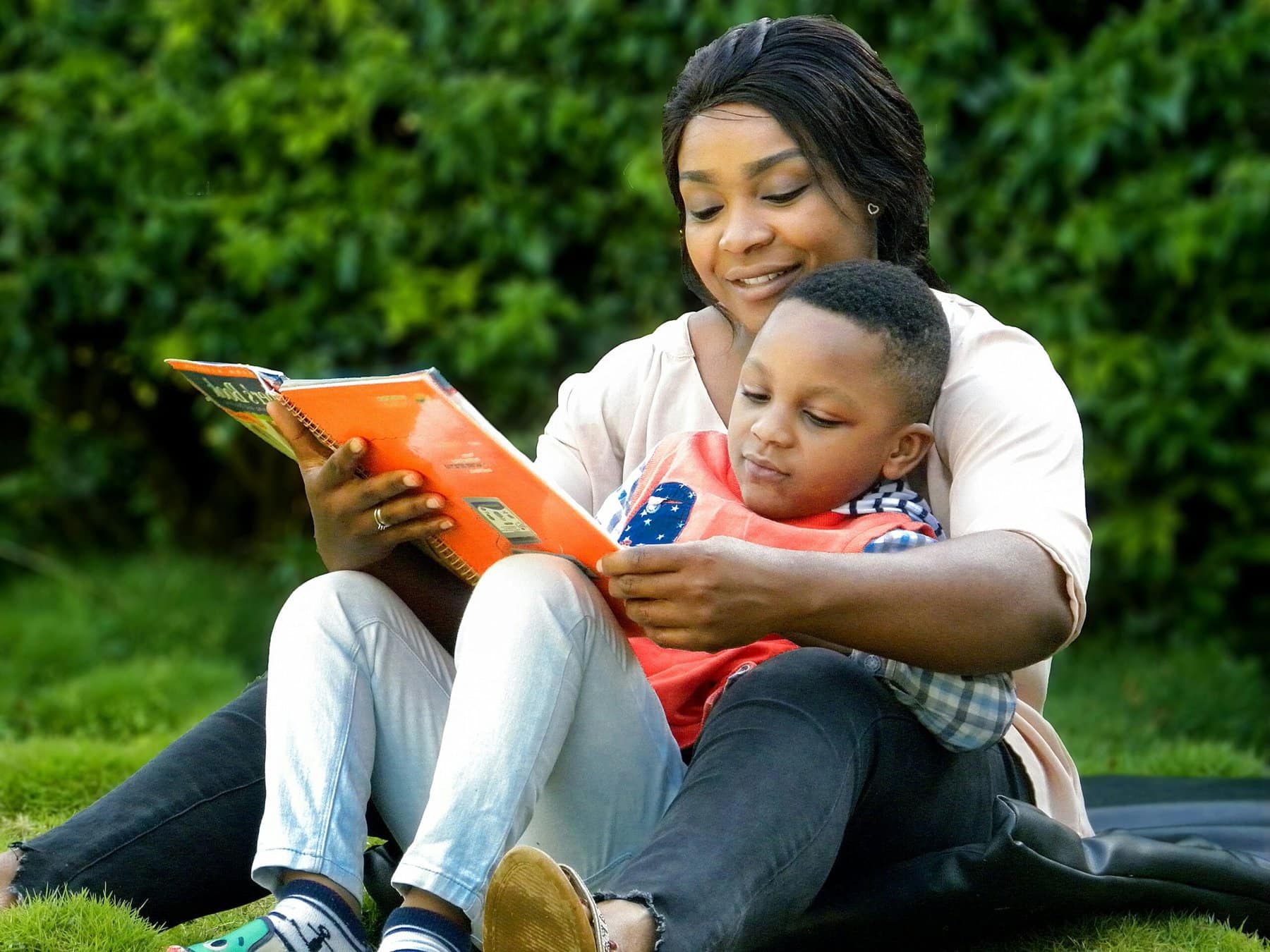 A mother sits comfortably on the floor reading with her child