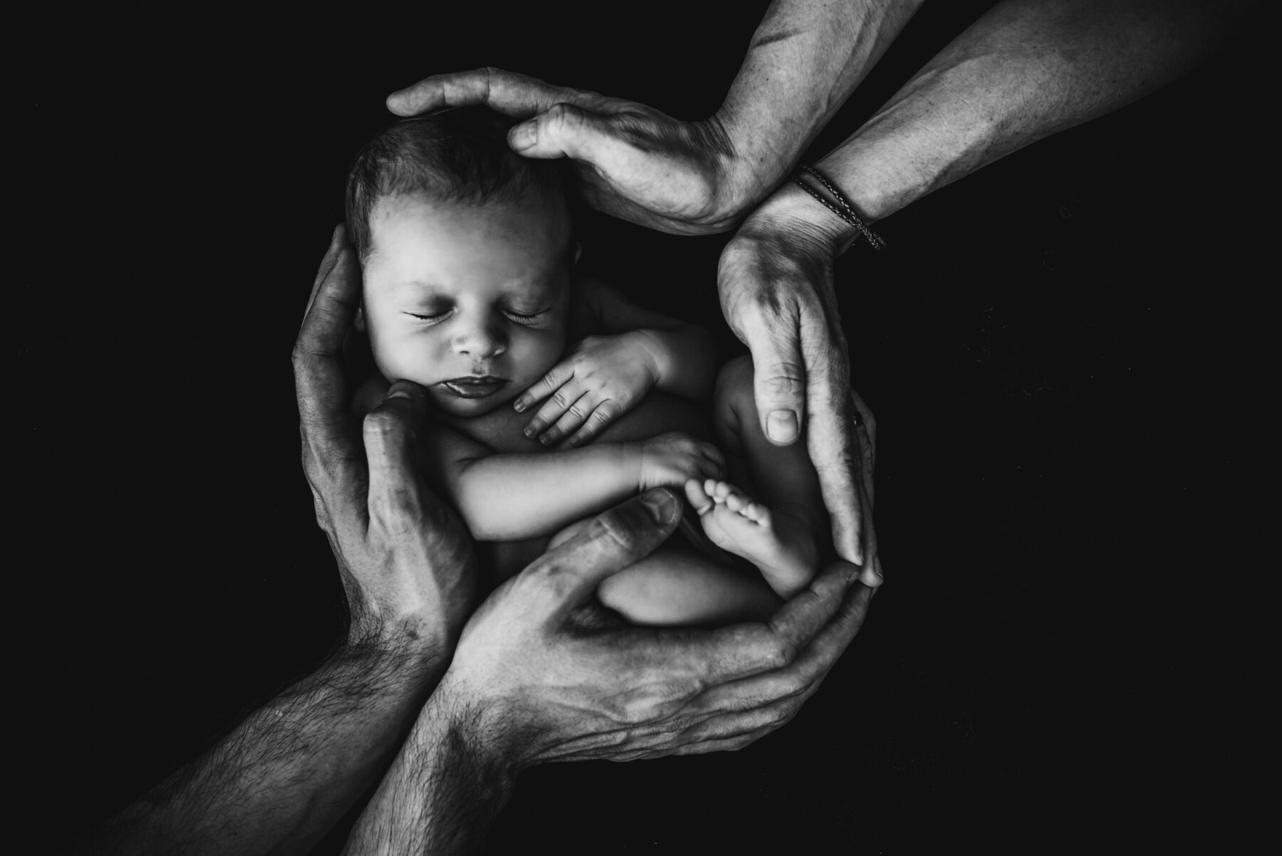 Newborn baby sleeping peacefully, cradled and supported by several pairs of hands.